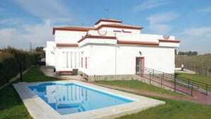 A white building with a swimming pool, a red door, and a stone base. - Rural House Jardin del Arroyo. (El Viso de San Juan)