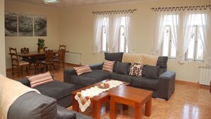 A living room with a sofa set, a dining table with chairs, and a view of the outside through large windows. - Rural House Jardin del Arroyo. (El Viso de San Juan)
