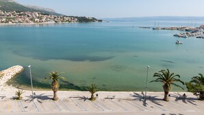 Una marina costera con aguas cristalinas, una playa de arena con palmeras y un pueblo al fondo.
