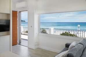 A living room with a large window overlooking a beach, a flat-screen TV mounted on the wall, and a wooden door leading to an outdoor area. - Mollarri apartment by Egona (Zarautz)