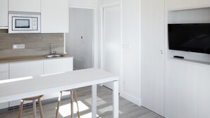 Una cocina moderna con armarios blancos, encimera de madera, microondas integrado, un fregadero y un televisor de pantalla plana montado sobre la encimera.