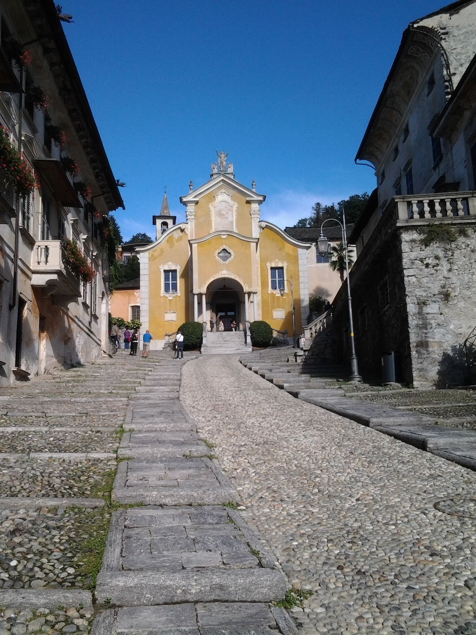 A cobblestone street leading to a yellow building with a bell tower.