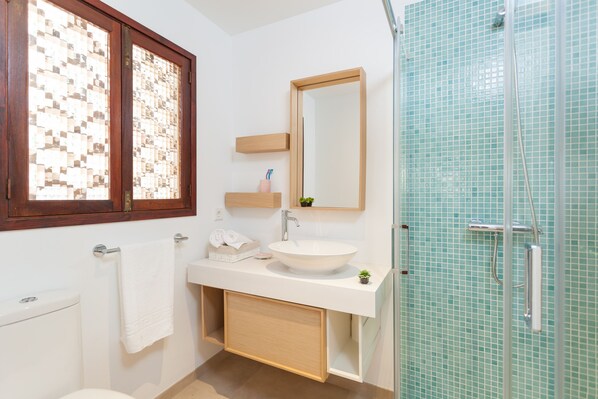 Un baño con lavamanos blanco, un espejo, toallero y zona de ducha con puertas de cristal.