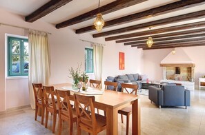 A dining area with wooden chairs and a table, a living room with sofas and a fireplace, and a kitchen area with a brick wall.