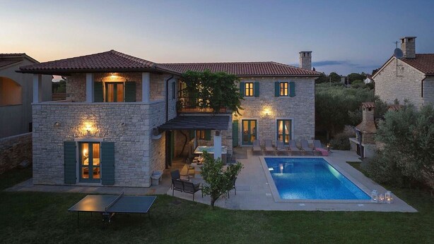 Uma casa de pedra de dois andares com piscina, área de estar ao ar livre e um pátio.