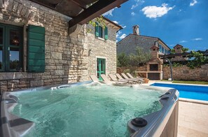 A stone building with a hot tub and lounge chairs.