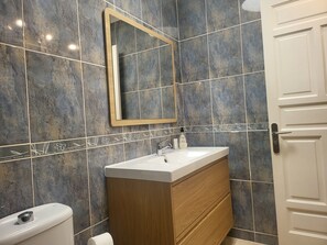 Ein Badezimmer mit einer Wand aus Marmorfliesen, einem Holzbadezimmermöbel, einem weißen Waschbecken und einer Toilette.