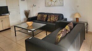 Un salon avec un canapé, une table basse, un téléviseur, une lampe et un tableau au mur.