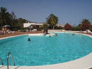 Ein Schwimmbecken mit mehreren Personen, Liegestühlen und Palmen.