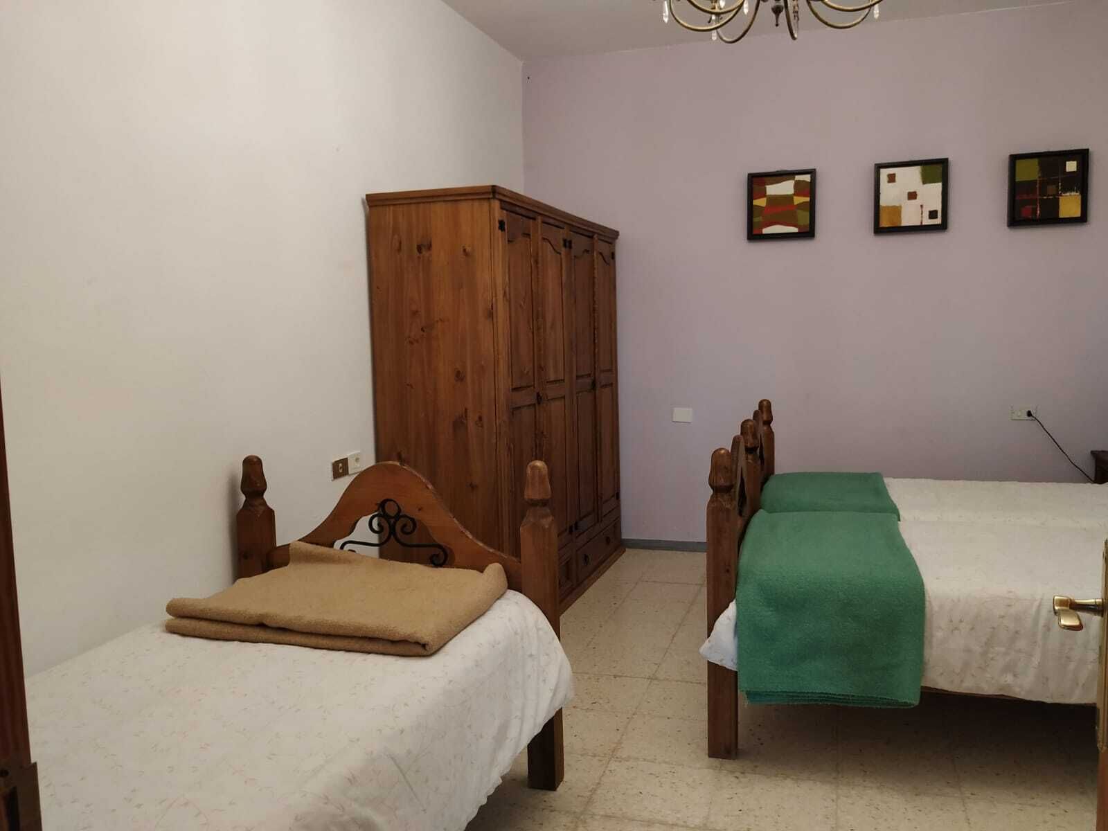 A bedroom with two wooden beds, a wardrobe, and three abstract paintings on the wall.