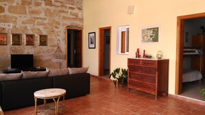 Un salon chaleureux avec un mur en pierre, un canapé noir, une commode en bois et un téléviseur.