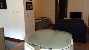 A modern living room with a glass-top table, a sofa, a television, and a small seating area with a table and chairs. - I Love Alegria - cosy Studio (Porto)