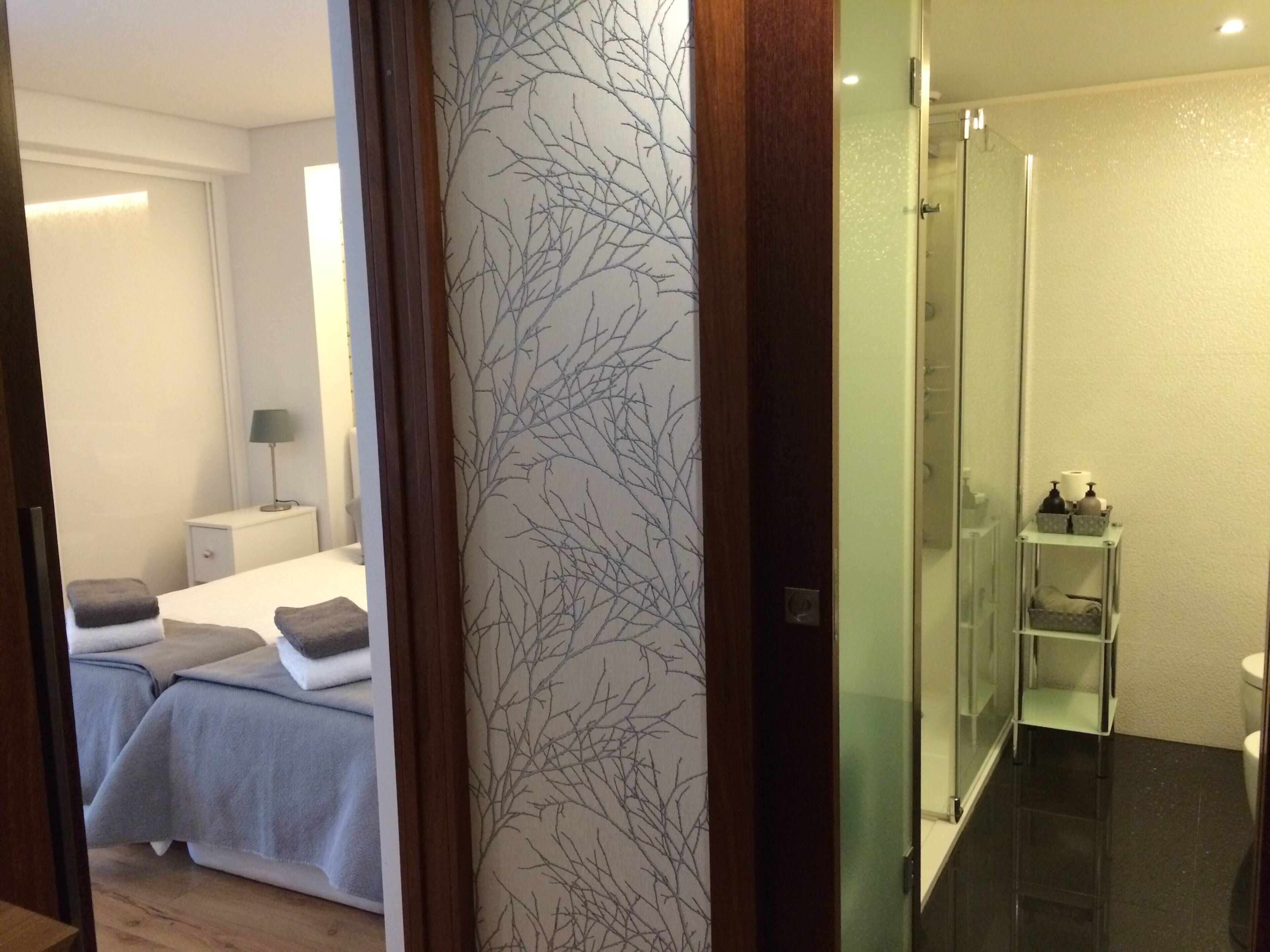 A hotel room with a bed, bedside table, lamp, and a bathroom with a shower and toilet.