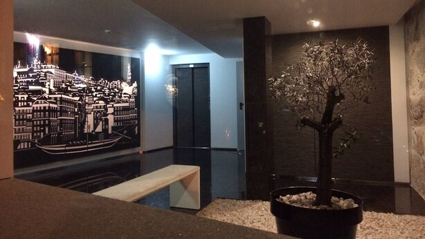 A modern interior with a cityscape mural, a potted tree, and a bench. - I Love Alegria - cosy Studio (Porto)