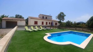 A swimming pool with a surrounding lawn and lounge chairs, a house with a tiled roof, and a wooden fence. - Cozy, quiet house with Pool, Wifi and sea view (Son Servera)