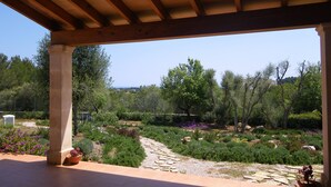 An outdoor patio area with a pergola structure, stone pathway, and various plants and shrubs. - Cozy, quiet house with Pool, Wifi and sea view (Son Servera)