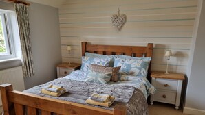 A bedroom with a wooden bed, two bedside tables, a nightstand, a window with curtains, and a wall-mounted heart decoration. - 2 Bedroom Luxury Cottage close to Bakewell, in the stunning Peak District (Over Haddon)