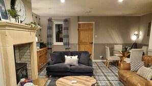 A cozy living room with a fireplace, a sofa, a coffee table, and a dining area with chairs. - 2 Bedroom Luxury Cottage close to Bakewell, in the stunning Peak District (Over Haddon)