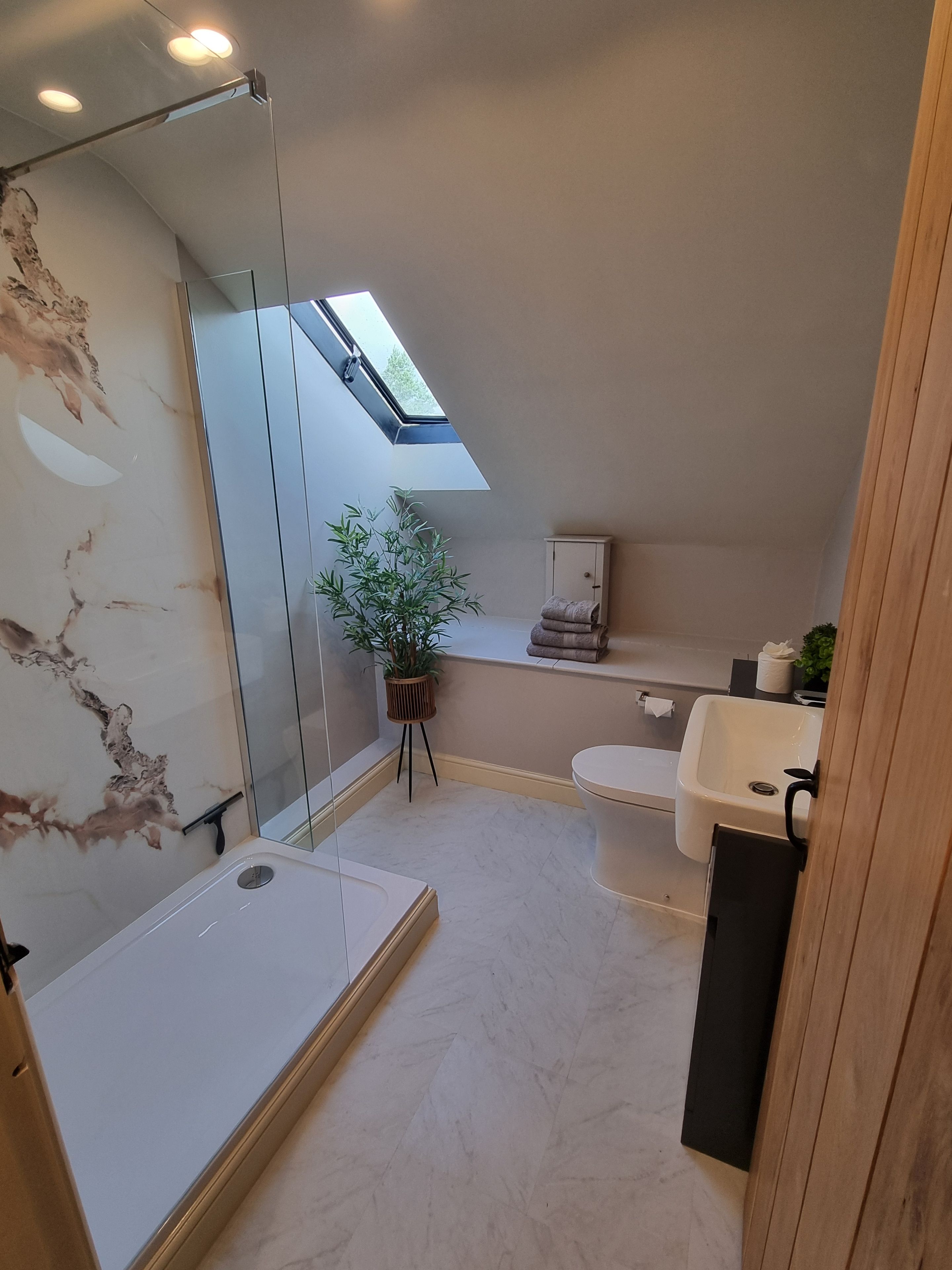 A modern bathroom with a skylight, a shower, a sink, and a toilet.