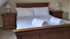 Een slaapkamer met een houten bed, witte lakens, twee nachtkastjes met lampen, een plafondlamp en een dromenvanger.