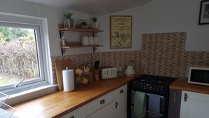 Een keuken met houten aanrechtbladen, witte kasten, een gasfornuis, een magnetron en een raam met uitzicht op bomen.