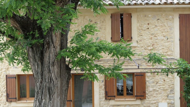 A stone building with wooden shutters, a door with a glass panel, and a table with chairs in front. - Character house in the heart of the Luberon Park (Gargas)