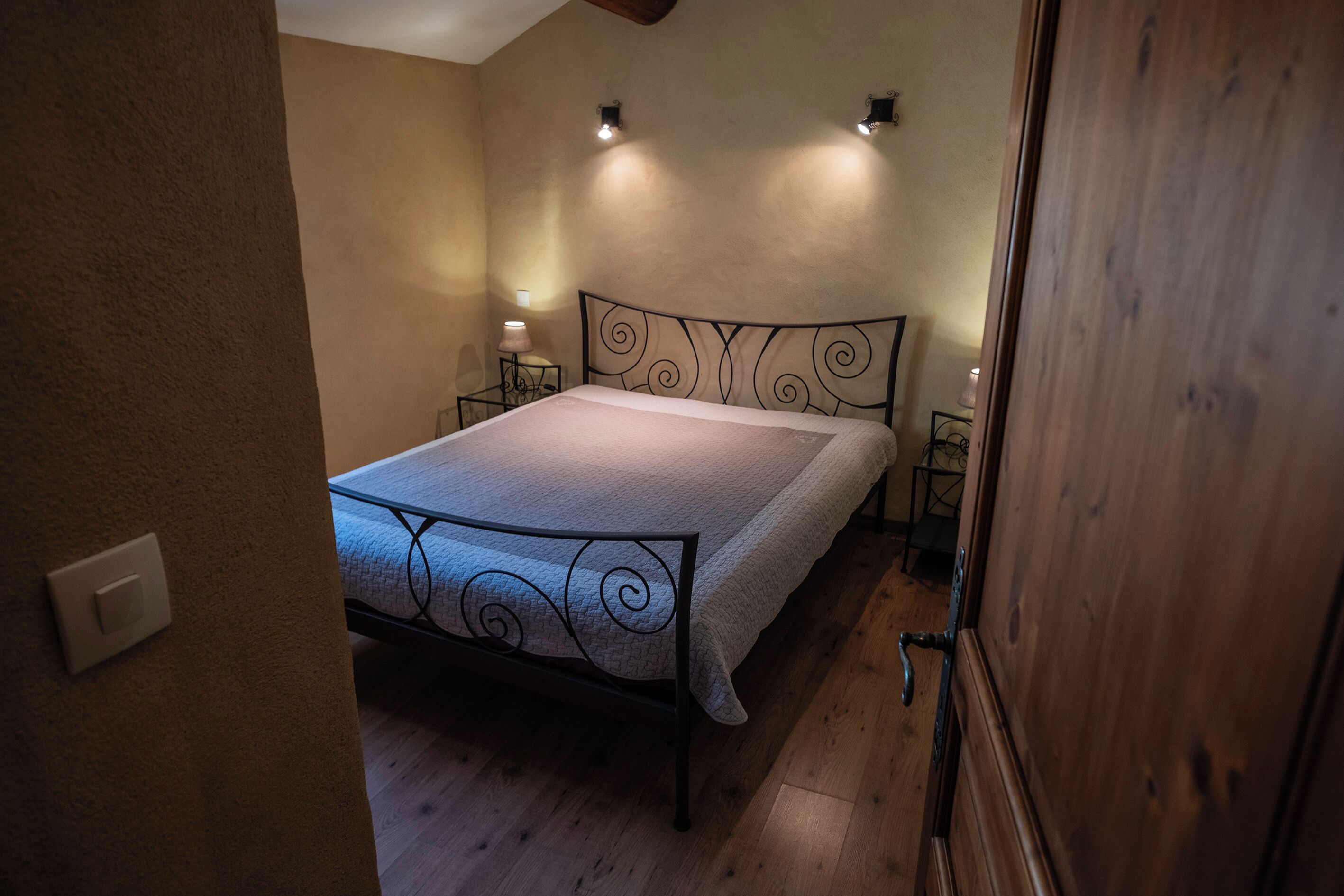 Een slaapkamer met een metalen bedframe, een houten vloer en twee bedlampjes.