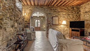 A stone-walled room with a sofa, a television, and a bookshelf. - Country House & Spa - Inside Nature with panoramic views, Art Surrounded (Volterra)