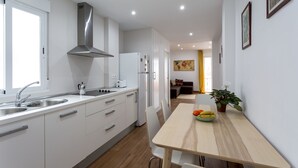 A modern kitchen with white cabinetry, stainless steel appliances, and a wooden dining table with a bowl of fruit.