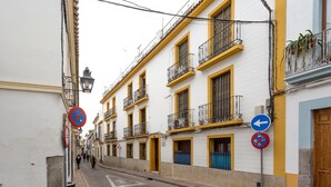 A narrow street with white and yellow buildings, a no parking sign, and a directional sign.