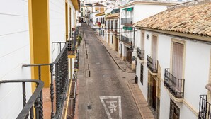 A narrow street lined with white buildings with yellow balconies and red flowers.