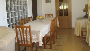 Un comedor con una mesa larga, sillas de madera, mantel de encaje blanco y un frutero.