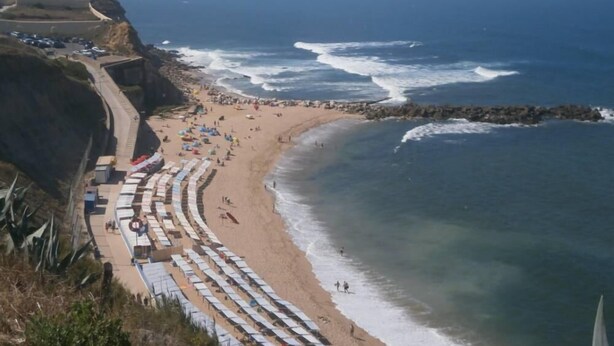 Una playa costera con hileras de tumbonas y sombrillas, un litoral rocoso y una vista despejada del océano.