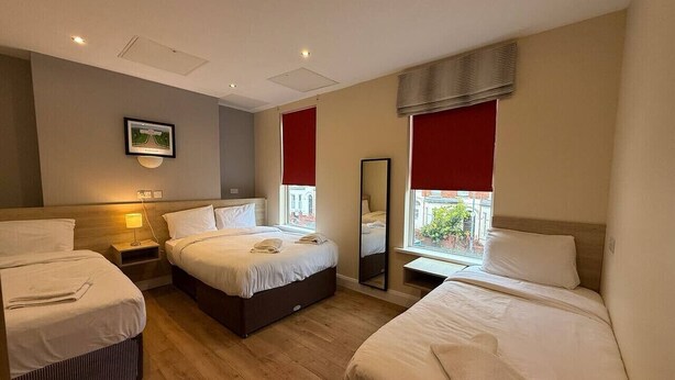 A hotel room with three beds, a large mirror, and a window with red curtains. - The Townlets Townhouse - 5BR - sleeps 13 (Belfast)