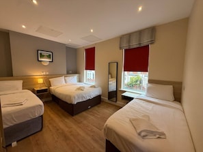 Une chambre d’hôtel avec trois lits, un grand miroir et une fenêtre avec des rideaux rouges.