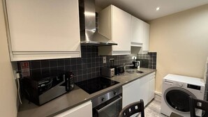 A compact kitchen with a built-in stove, oven, and microwave, a washing machine, and a dining area with a table and chairs. - The Townlets Townhouse - 5BR - sleeps 13 (Belfast)