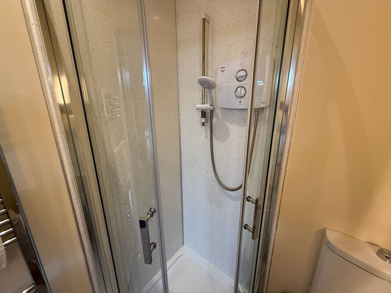 A glass-enclosed shower stall with a handheld showerhead and control panel.