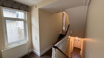 A staircase with a wooden handrail and white balusters, leading to a landing with a radiator and a window with a decorative valance.