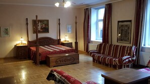 A traditional bedroom with a four-poster bed, a wooden bench, a striped sofa, and a small table. - SUNNY LOUNGE GRAND APARTMENT (Riga)