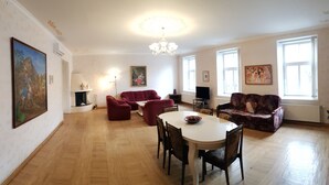 A spacious living room with a round dining table, red sofas, and a chandelier. - SUNNY LOUNGE GRAND APARTMENT (Riga)