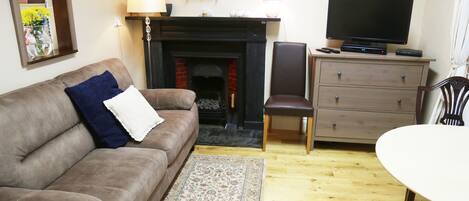 A living room with a brown sofa, a patterned rug, a fireplace, a television, and a wooden cabinet.