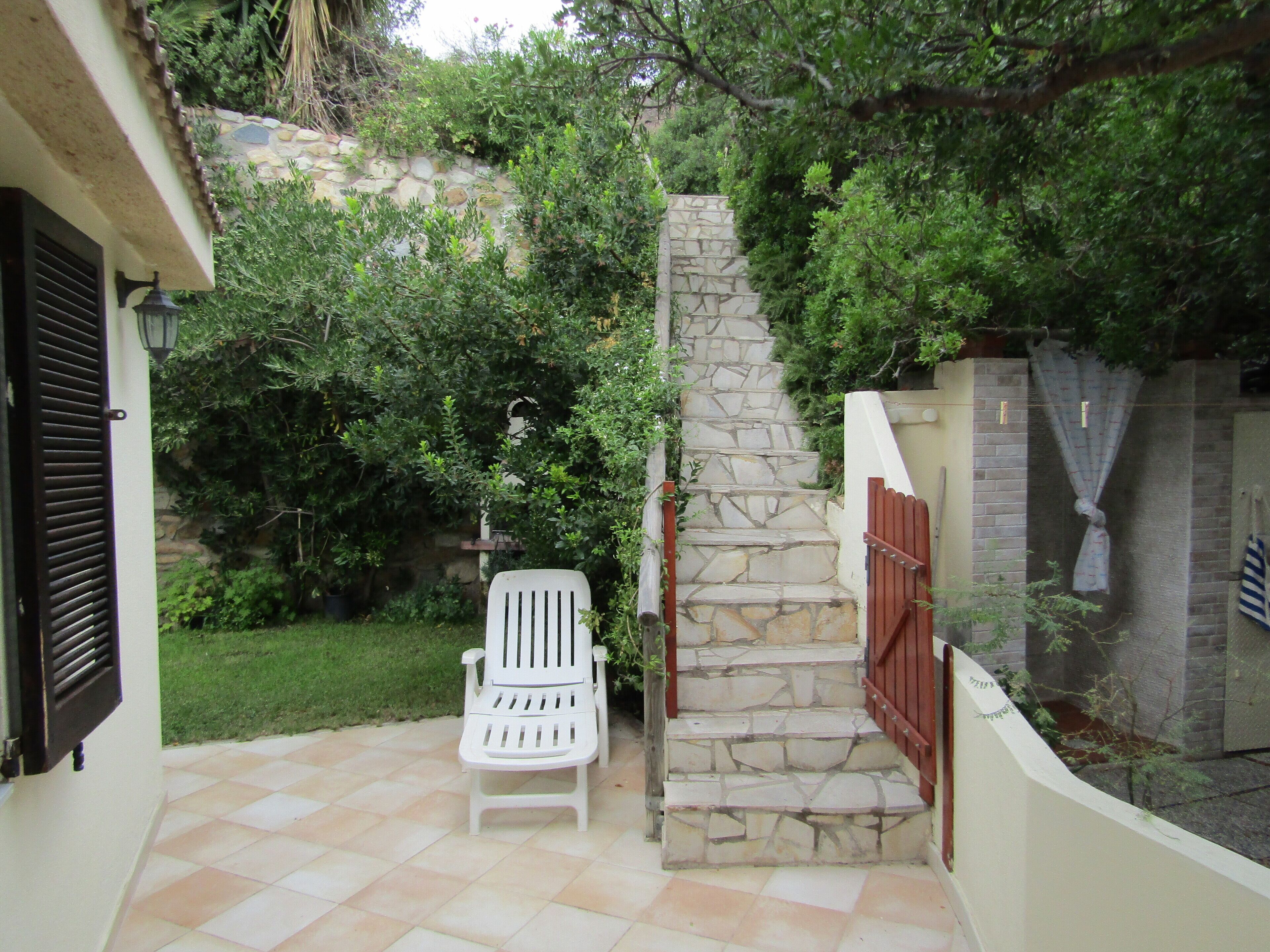 A patio with a white chair, stone steps, and a stone wall.