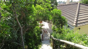 A narrow stone pathway flanked by lush greenery, leading to a building with a tiled roof. - House / Villa - independent  with beautiful sight on the gulf (Costa Rei)