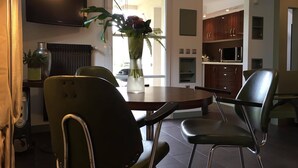 A modern dining area with a round table, two chairs, a vase with flowers, a television, and a kitchen in the background. - Cottage in the countryside, less than 10 minutes from Mulhouse center, near Switzerland (Steinbrunn-Le-Bas)