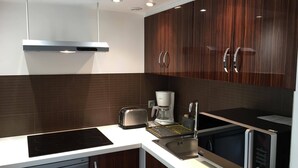 A modern kitchen with dark wood cabinets, a stainless steel range hood, a toaster, a coffee maker, and a microwave. - Cottage in the countryside, less than 10 minutes from Mulhouse center, near Switzerland (Steinbrunn-Le-Bas)