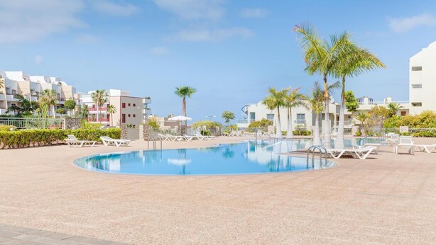 A pool area with lounge chairs and palm trees, surrounded by multi-story buildings.