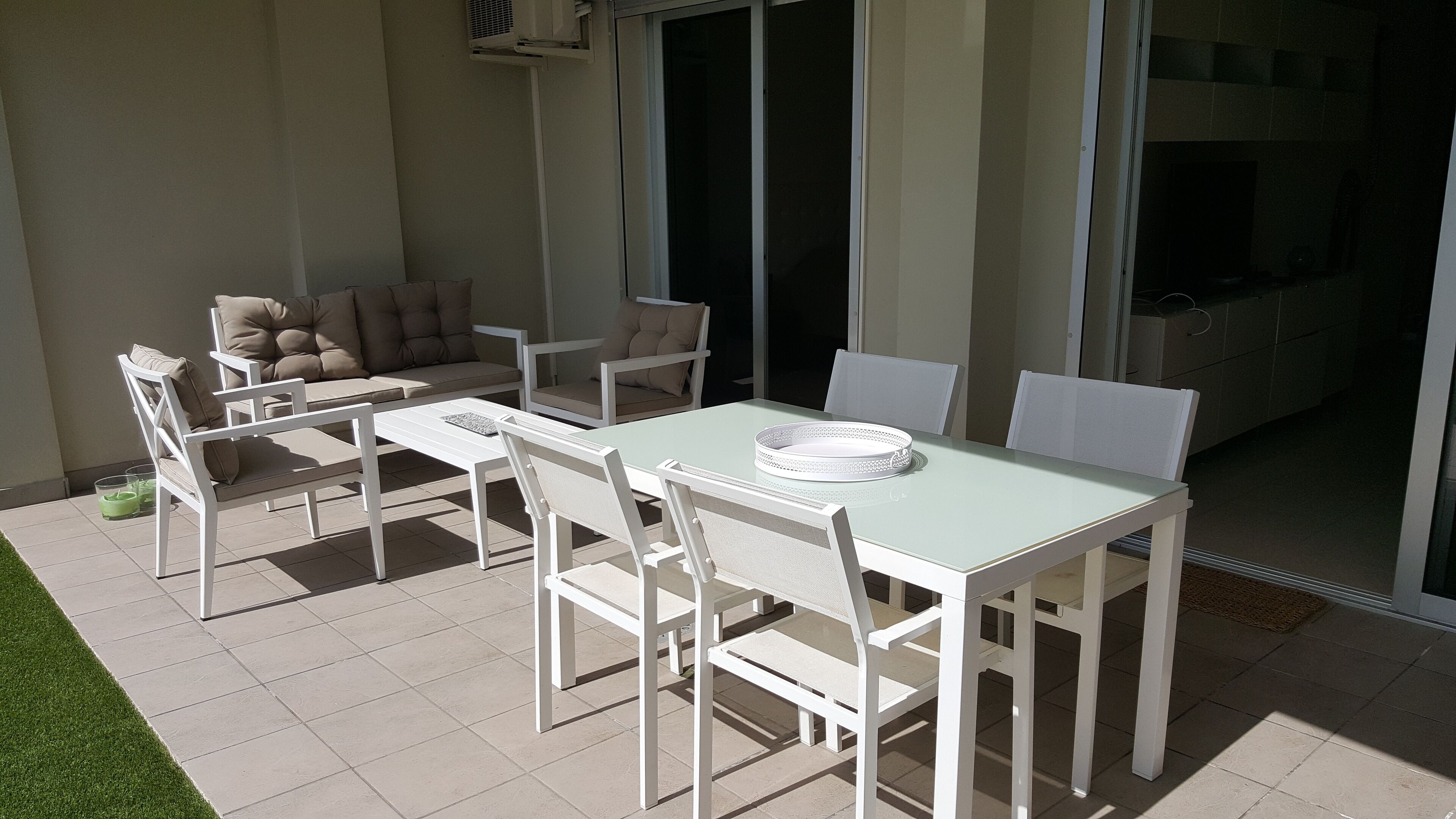 An outdoor patio with a white table and chairs, a sofa, and a sliding glass door leading to a balcony.