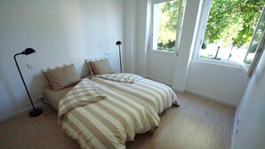 Ein Schlafzimmer mit einem Bett, zwei Nachttischlampen und einem Fenster mit Blick ins Grüne.