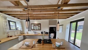 A spacious kitchen with a large island, wooden beams, pendant lights, and a view to the outdoors. - Stunning  country Cottage in Westfield, East Sussex. (Westfield)