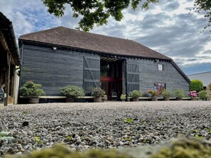 A rustic barn-style building with a gravel driveway and potted plants.